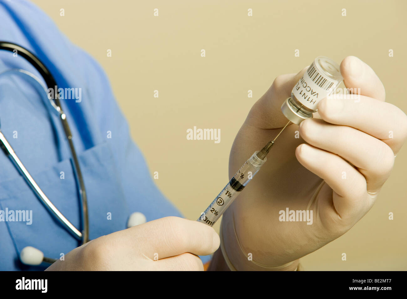 Male doctor or nurse wearing blue scrubs, stethoscope and gloves holding vial of H1N1 Swine Flu vaccine and syringe. Stock Photo