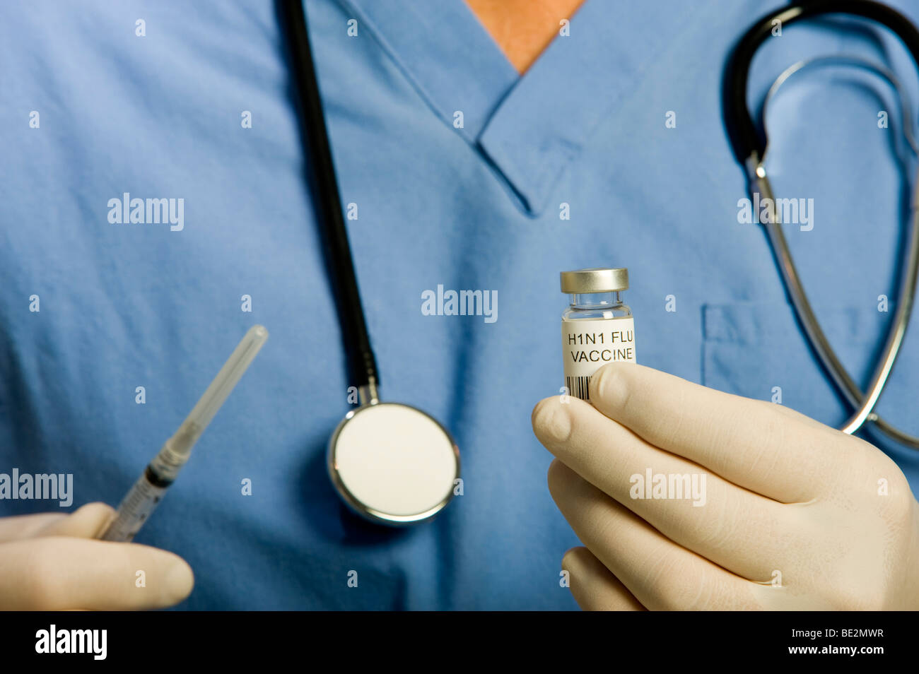 Male doctor or nurse wearing blue scrubs, stethoscope and gloves holding vial of H1N1 Swine Flu vaccine and syringe. Stock Photo