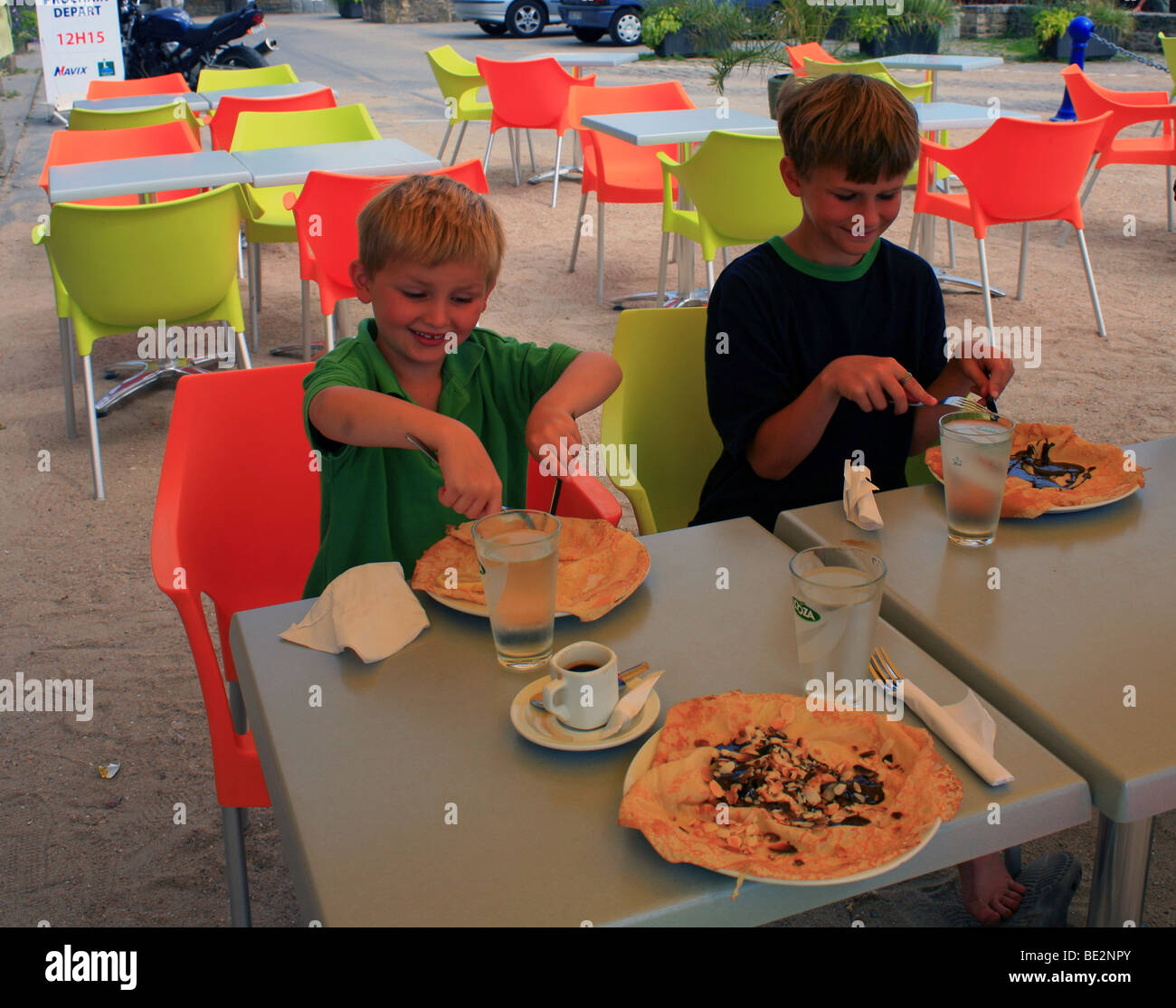 Two boys eating pancakes (crepes) outside cafe at Place Darioirgum, Locmariaquer, Morbihan