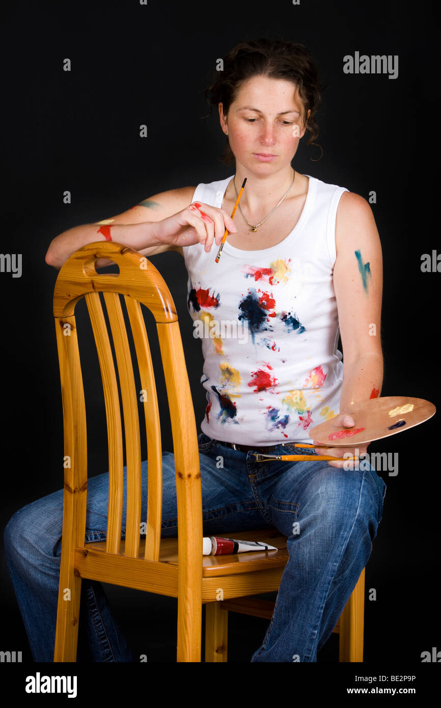 Artist sitting on a chair, holding a brush and colour palette, pensive Stock Photo