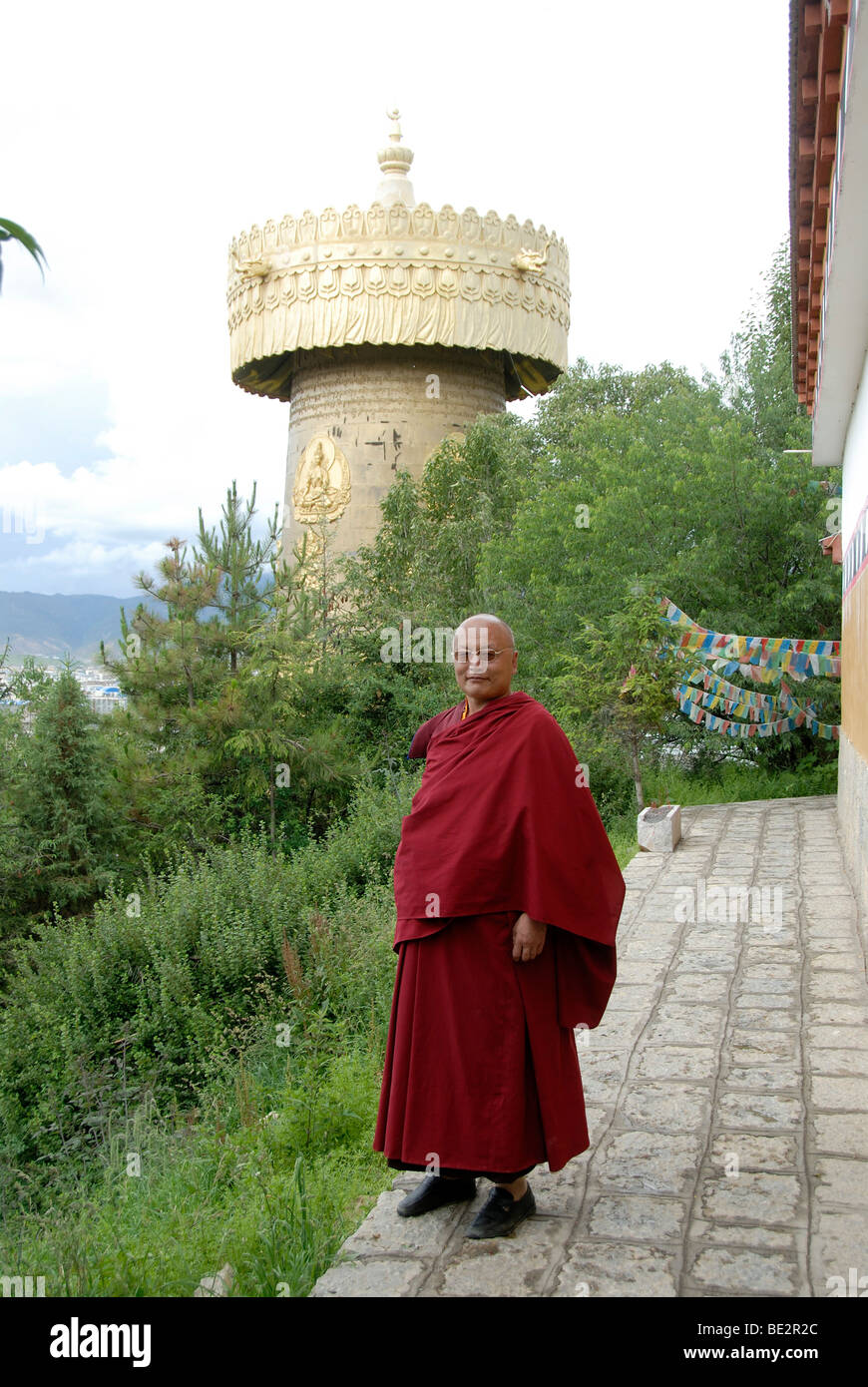 Tibetan Buddhist monk in a red robe, in front of a large prayer wheel