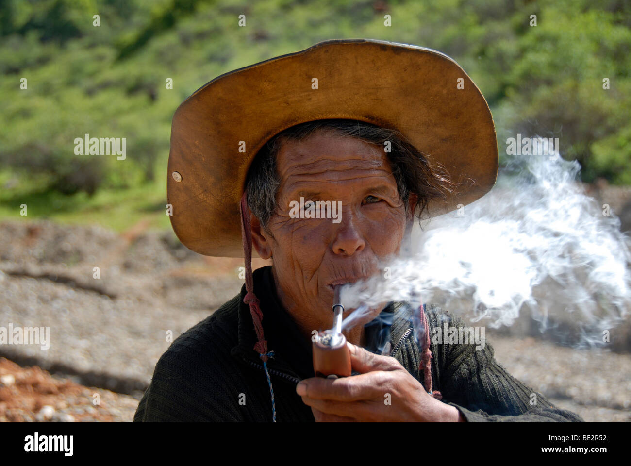 Portrait, ethnology, man of the Mosu ethnicity with hat, smoking a pipe, Yongning, Lugu Hu Lake area, Yunnan Province, People's Stock Photo