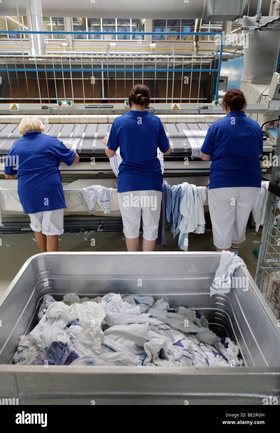 In the mangle room, from right to left, Nicole Haberstich, Amelie Mariechal and Luise Amm placing handtowels in an industrial m Stock Photo