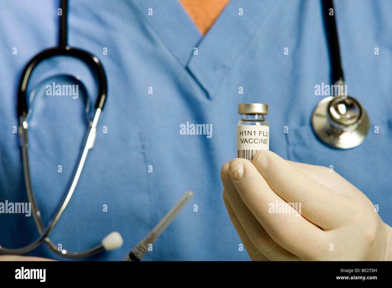 Male doctor or nurse wearing blue scrubs, stethoscope and gloves holding vial of H1N1 Swine Flu vaccine and syringe. Stock Photo