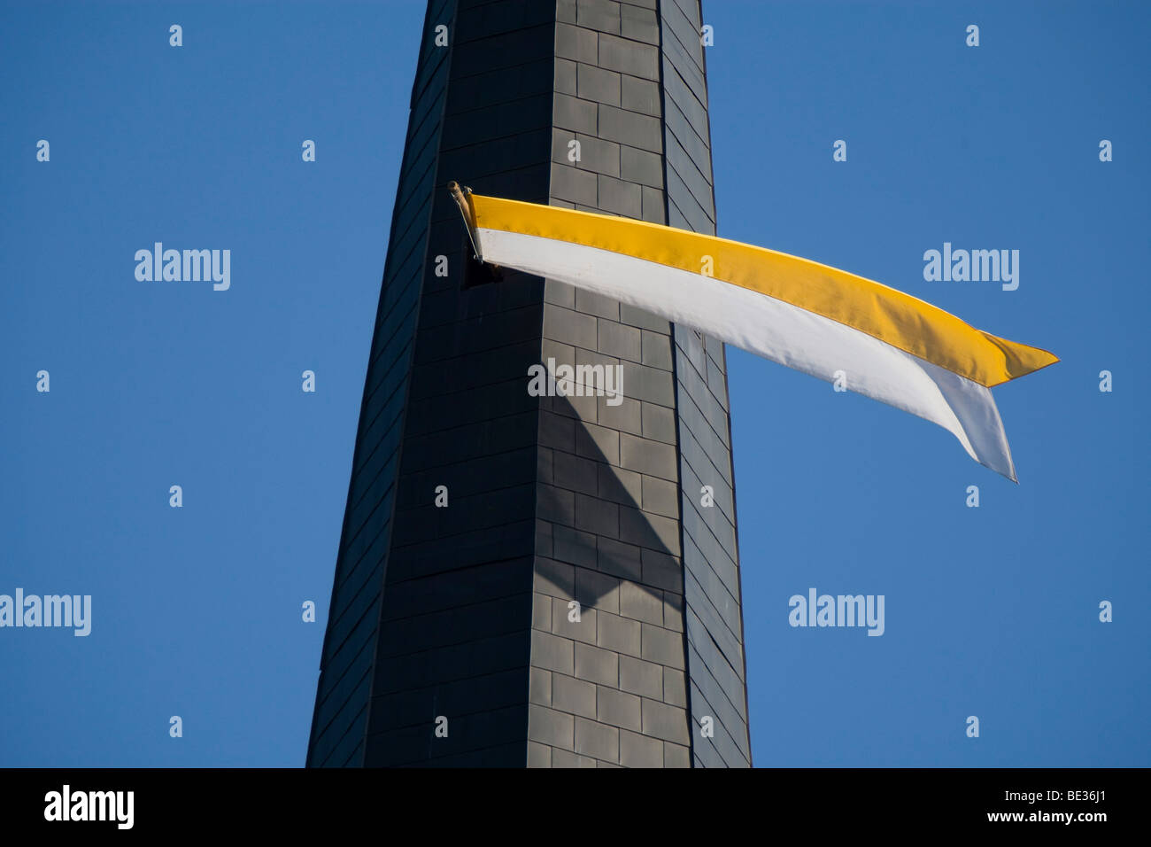 White and yellow flag fluttering from a church tower window against a steel blue sky Stock Photo