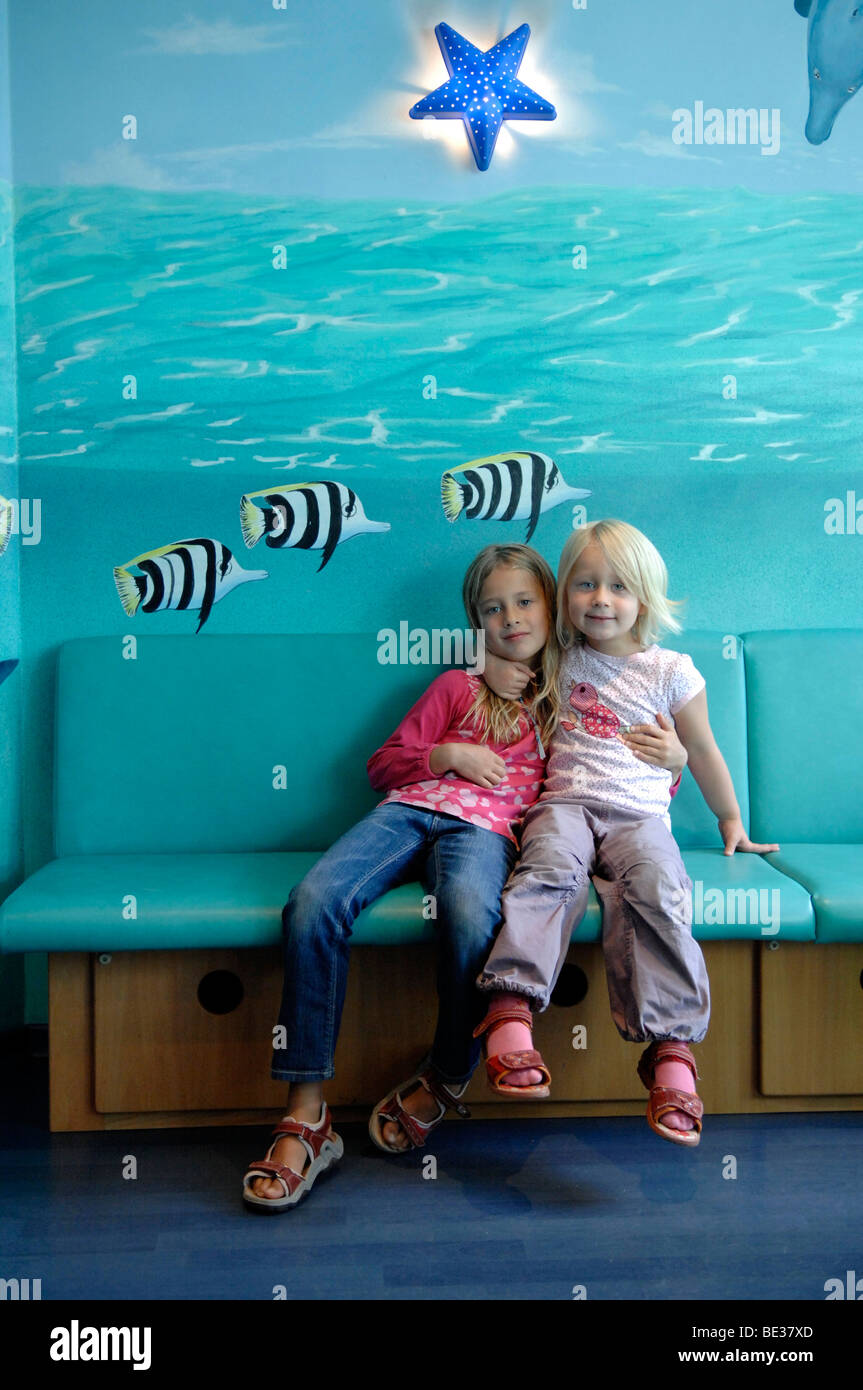 Two girls, sisters, on a bench in front of a painted wall Stock Photo