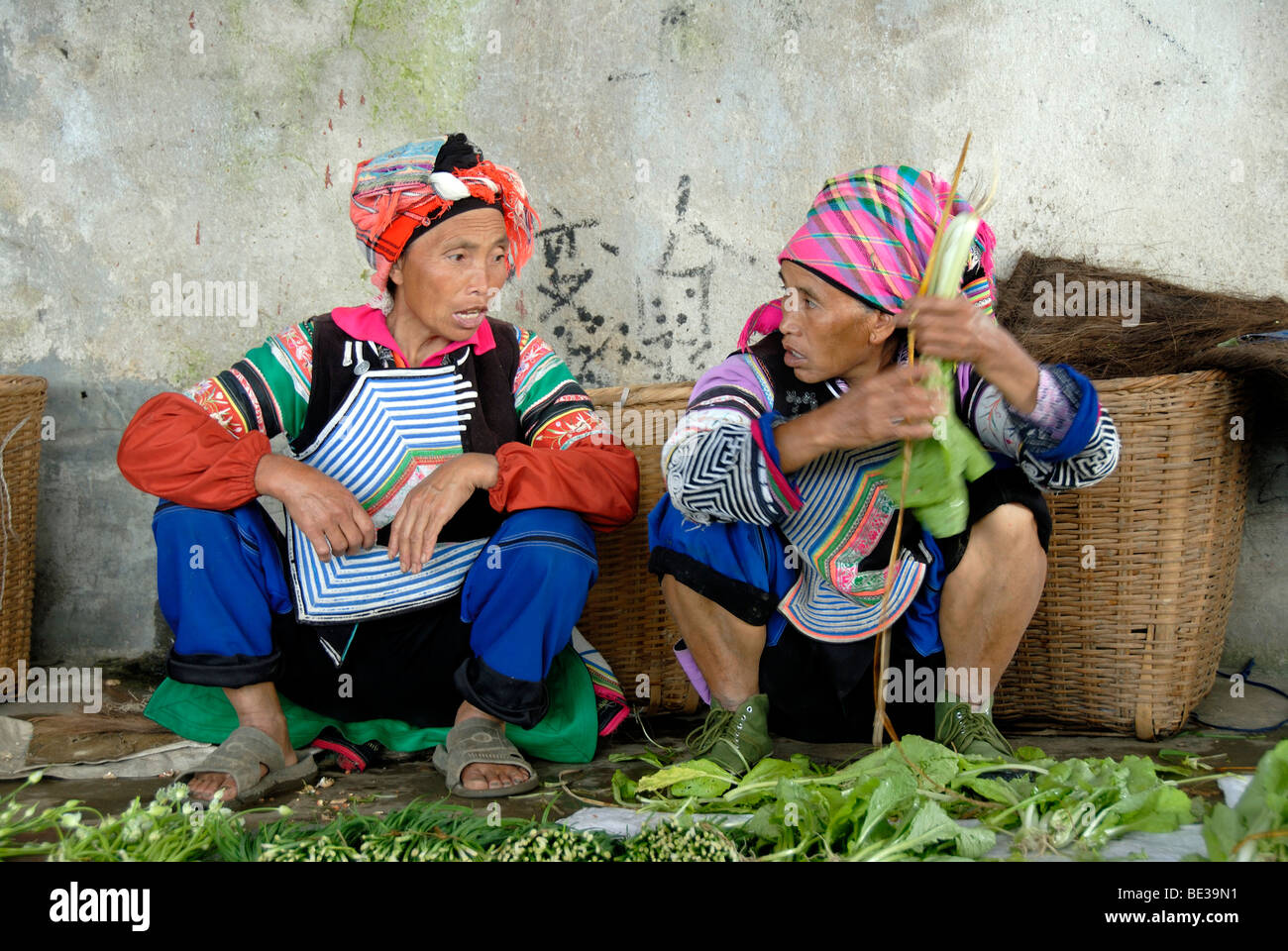 Ethnology, two market women of the Yi ethnic group squat deep in conversation, colorful clothes, Xinji, Yuanyang, Yunnan Provin Stock Photo