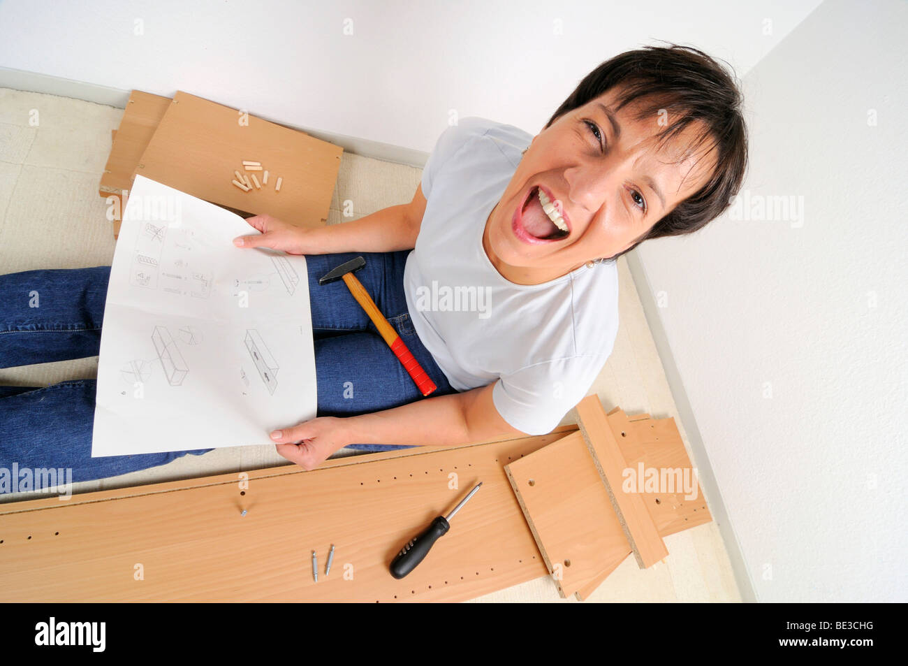Frustrated woman assembling furniture and screaming, reading the instructions Stock Photo