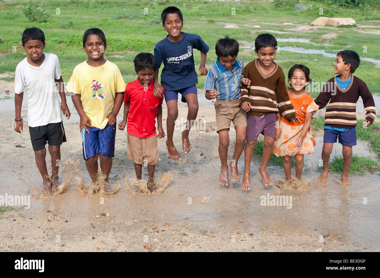 Indian children jumping and splashing in a puddle of water in the