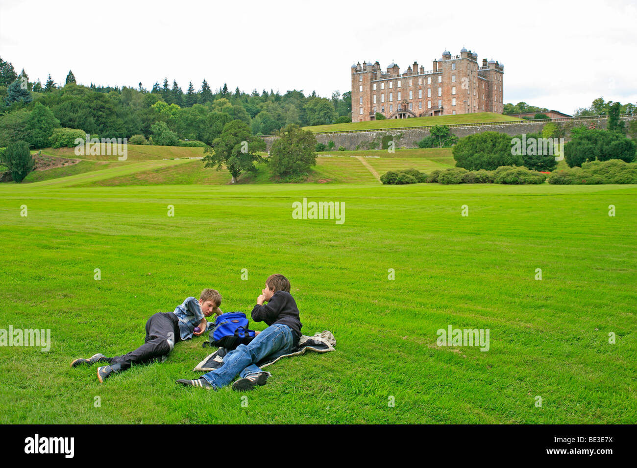 teenagers reclining on the lawn in front of Drumlanrig Castle near Carronbridge, Scotland, Great Britain Stock Photo