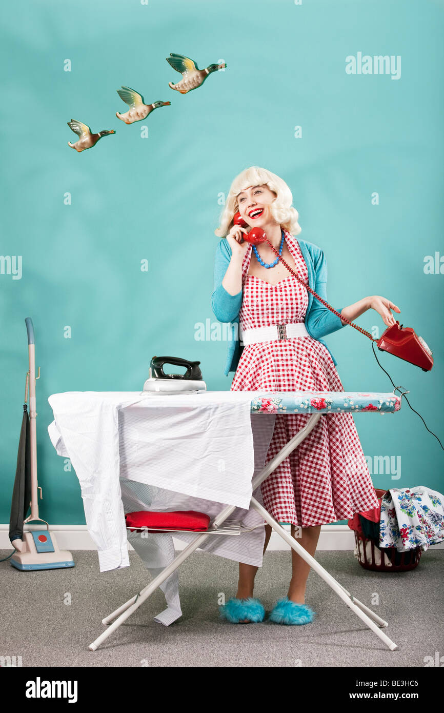 Retro image of 1960s housewife talking on the telephone whilst ironing Stock Photo