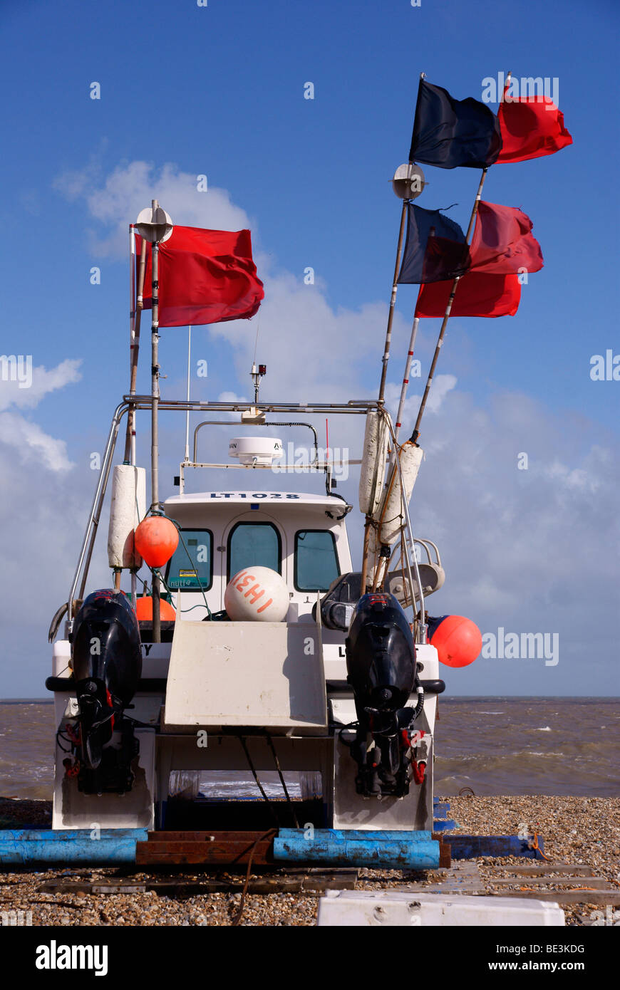 Fishing boat with lobster pot marker flags fluttering in strong wind, on the beach at Aldeburgh Stock Photo