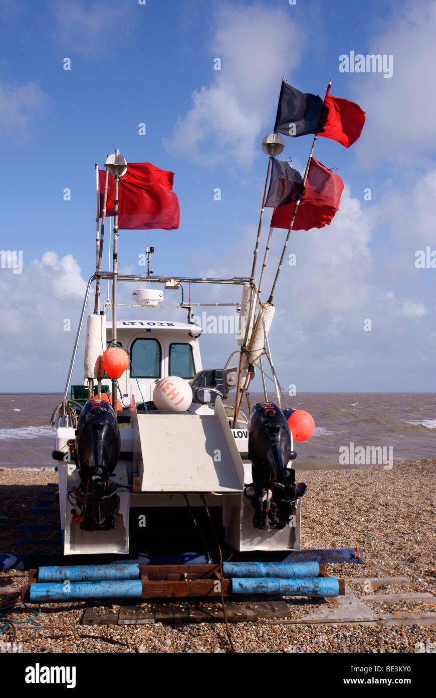 Fishing boat with lobster pot marker flags fluttering in strong wind, on the beach at Aldeburgh Stock Photo