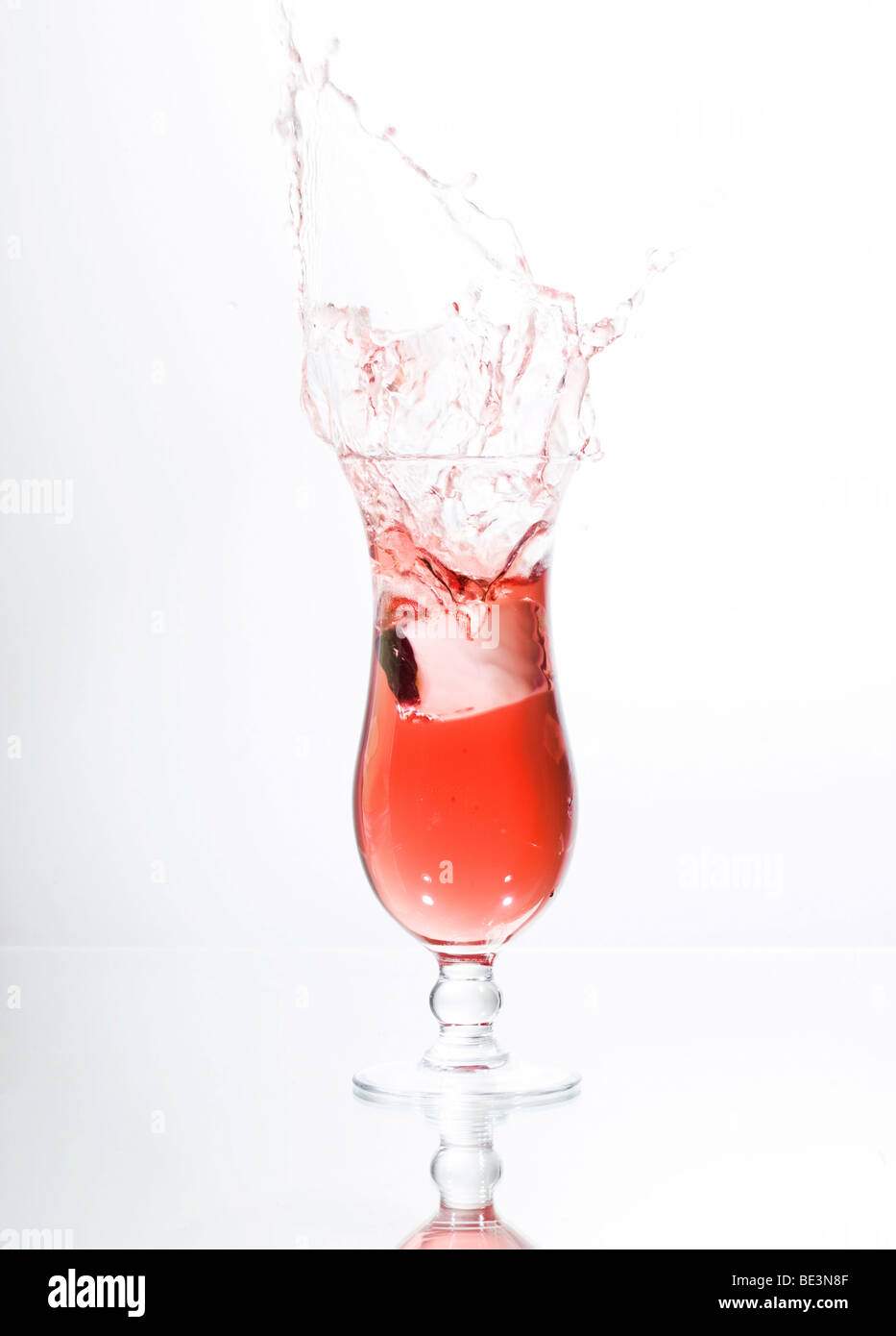 Ice cube falling into a glass of red liquid, juice, cocktail Stock Photo