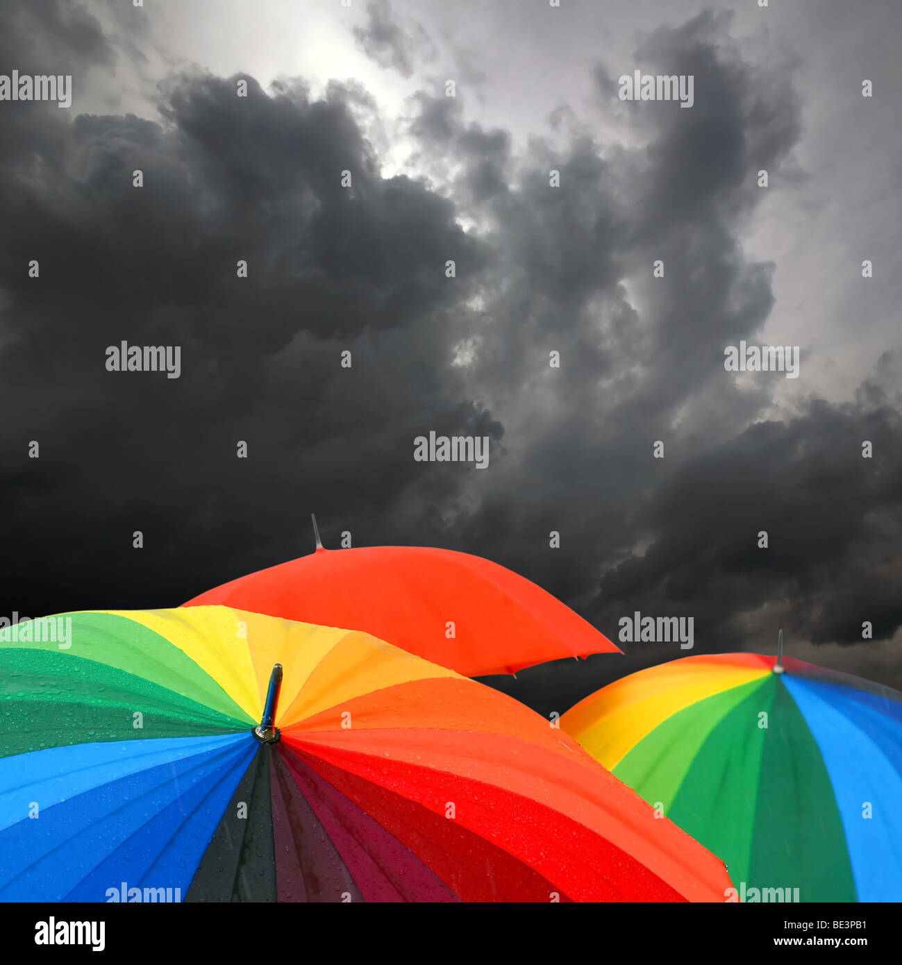 Rainbow colored umbrellas and dark cloudy sky in autumn time Stock Photo
