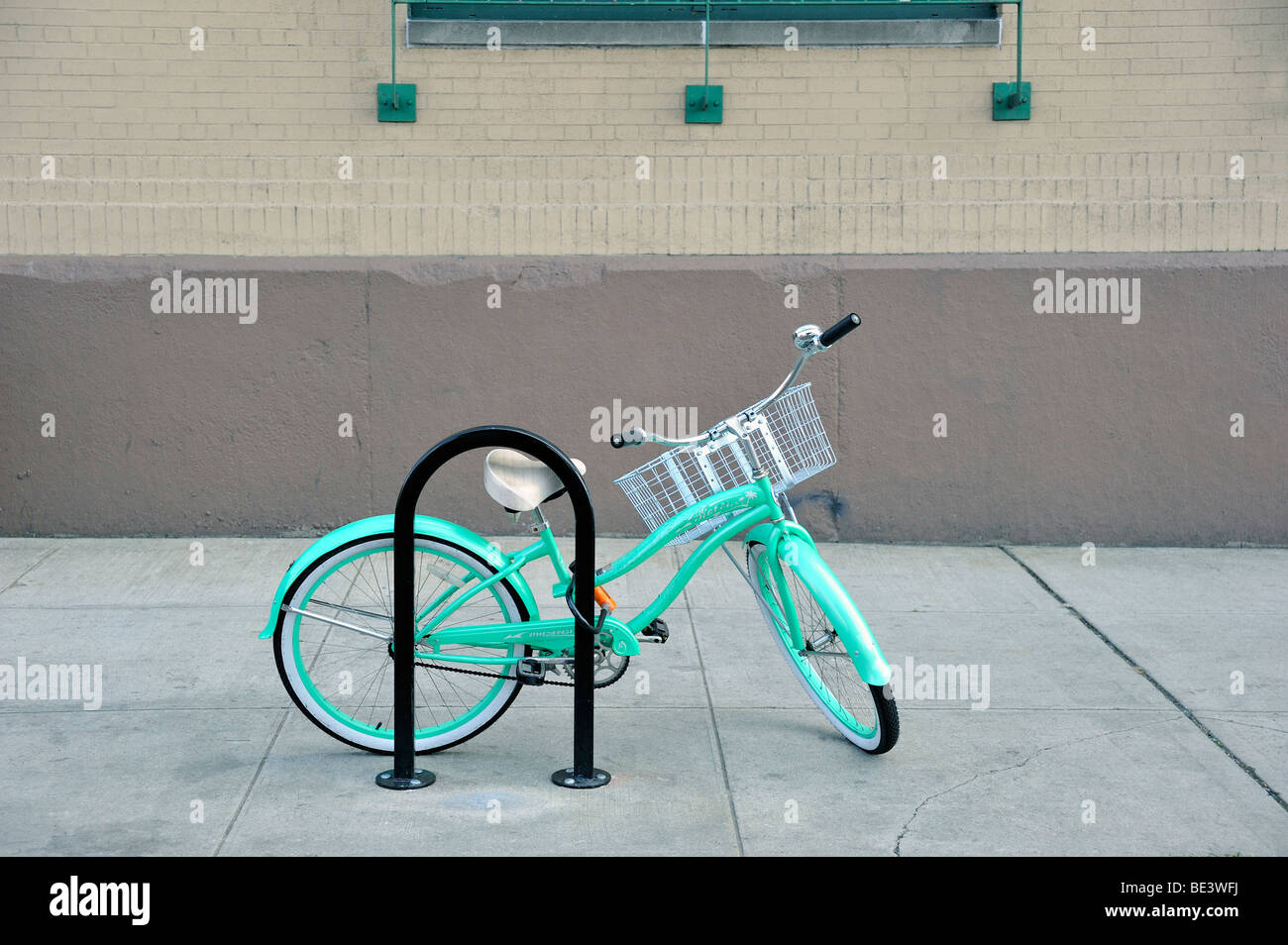 A women's turquoise green open frame Beach Cruiser style bicycle with a basket on the handlebars, locked to a bicycle stand in New York City Stock Photo