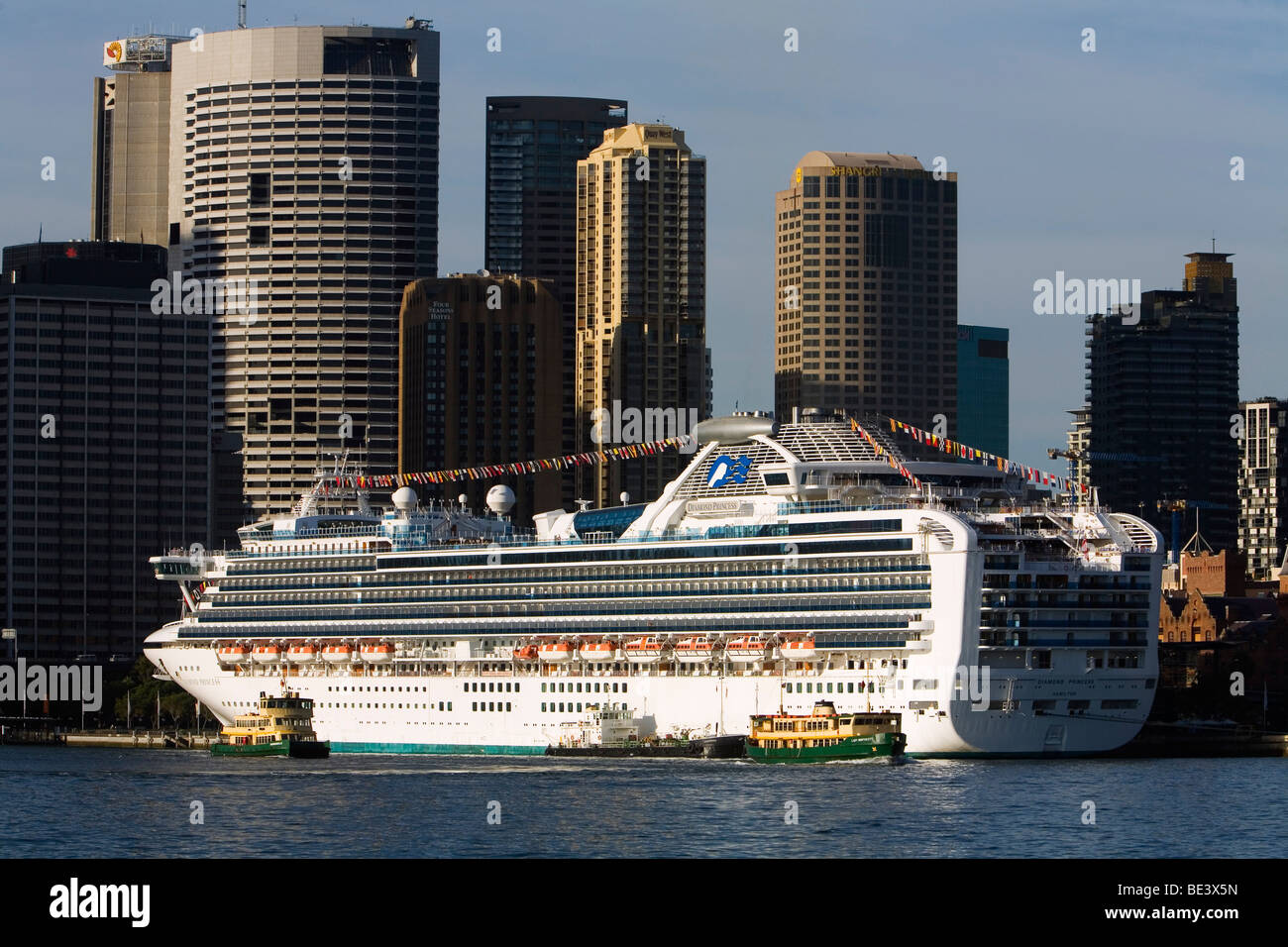 Sydney ferries are dwarfed by a cruise liner docked at the Overseas Passenger Terminal at Circular Quay. Sydney, New South Wales Stock Photo
