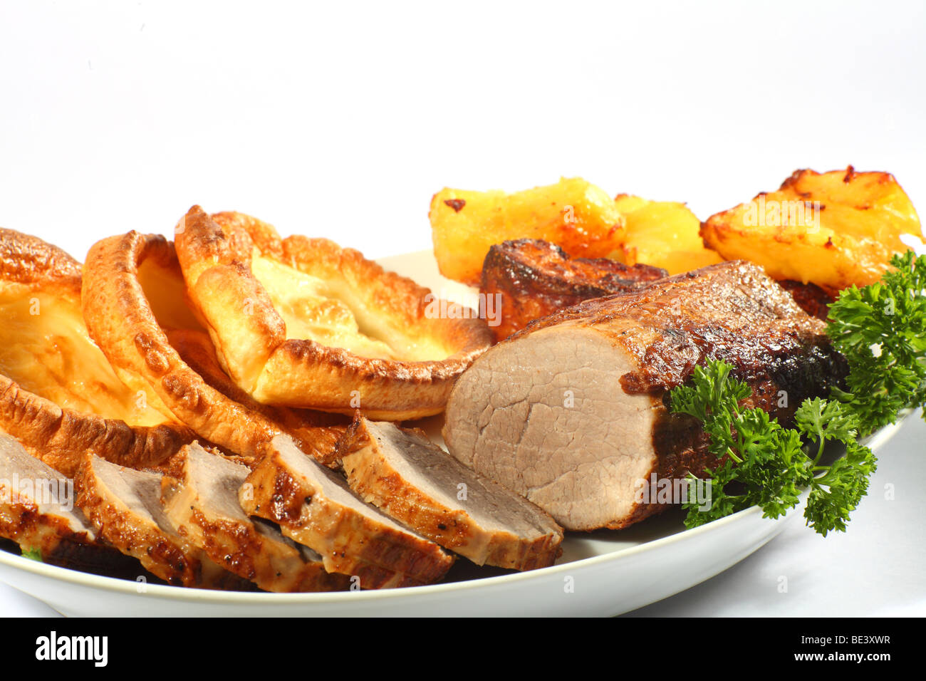 A serving dish of roast beef cut into thick medallions, with yorkshire