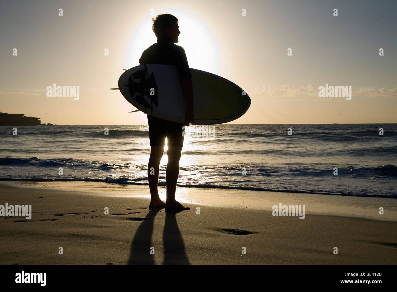 A surfer carrying surfboard is silhouetted by the morning sun.  Bondi Beach. Sydney, New South Wales, AUSTRALIA Stock Photo