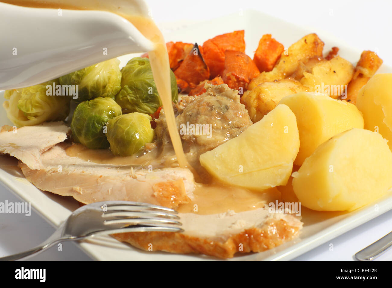 Pouring gravy on a festive turkey meal, with roast yams, roast parsnips, boiled potatoes and stuffing Stock Photo