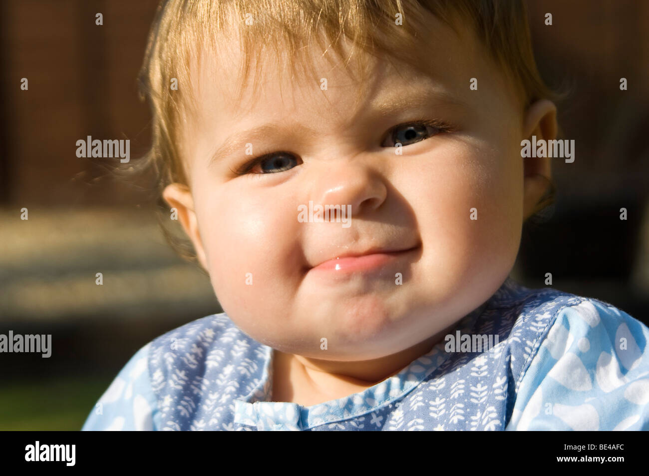 Horizontal close up portrait of a baby girl pulling funny faces and blowing raspberries in the sunshine. Stock Photo