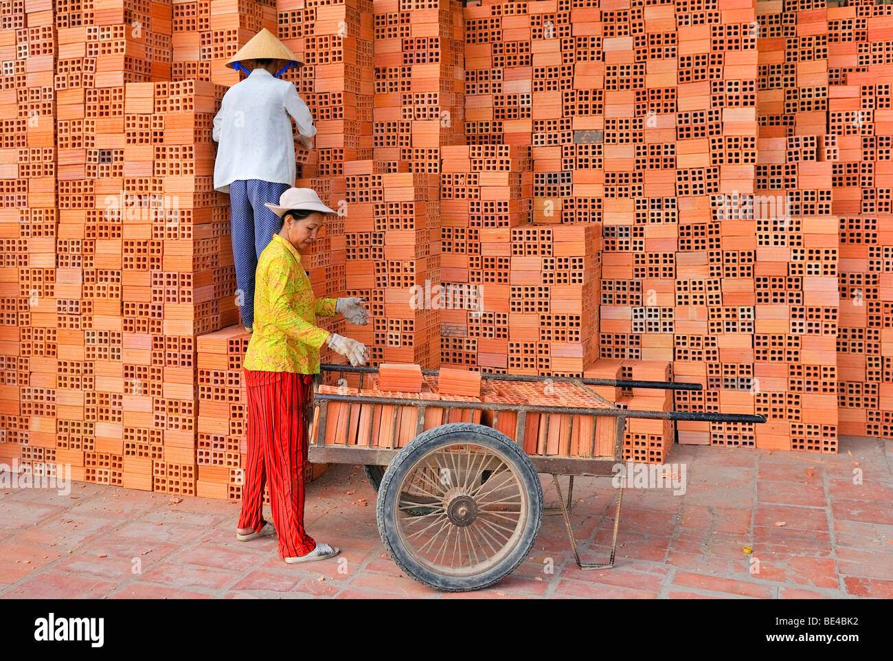 Two workers, women wearing traditional Vietnamese straw hats stacking bricks in a brick factory, Vinh Long, Mekong Delta, Vietn Stock Photo