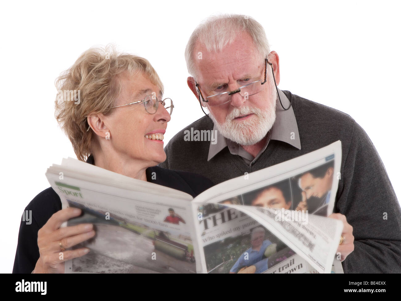 Older retired couple reading newspaper together, wife smiling at husband. Stock Photo