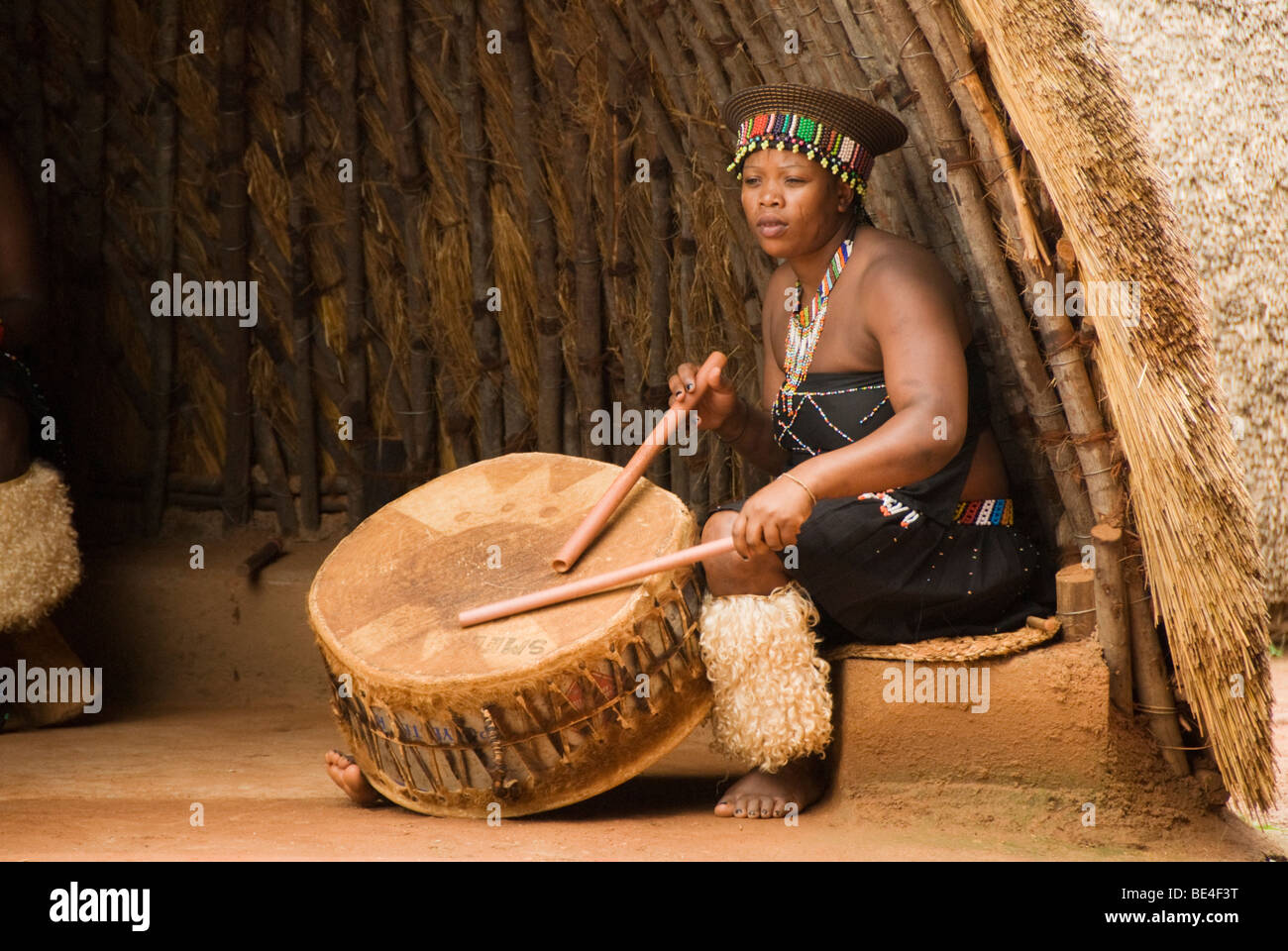 A Zulu maiden dressed in traditional dress beating a drum at the Phezulu Safari Park in The Valley of a Thousand Hills Stock Photo