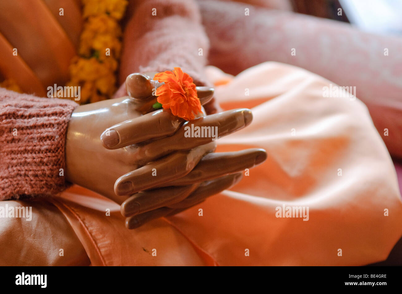 The hands of a statue of His Divine Grace A.C. Bhaktivedanta Swami Prabhupada holding a single flower. Stock Photo