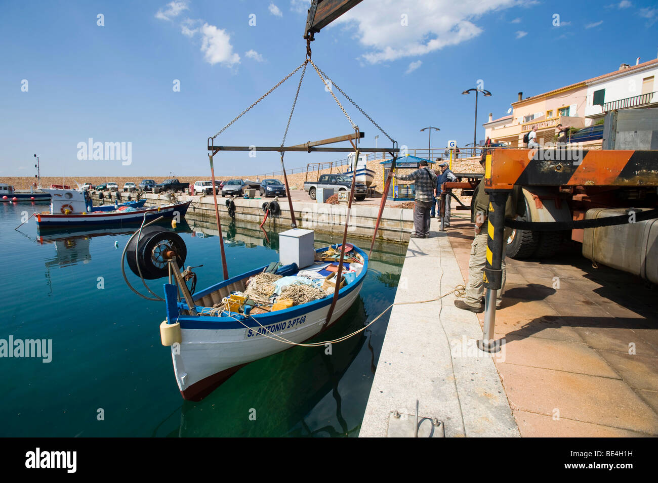 Fishing boat is being lowered into the harbor basin by a crane, Isola Rossa, Sardinia, Italy, Europe Stock Photo