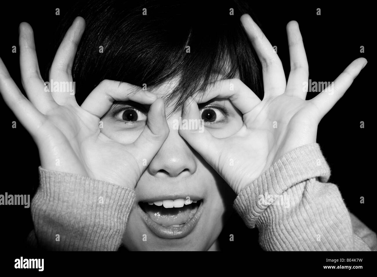 Quirky shot of a young Chinese woman making herself a pair of glasses with her hands. Stock Photo