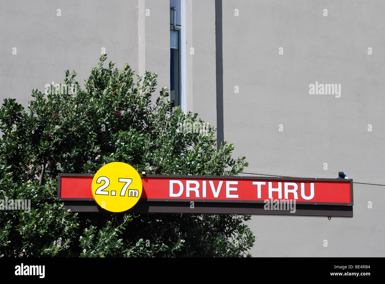 Drive through or 'drive thru' sign, protruding from bush with generic building in background. Stock Photo