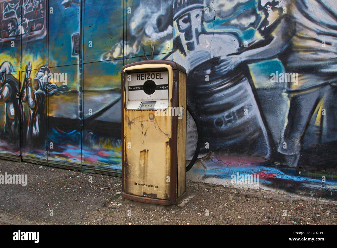 Old petrol pump for heating oil on derelict factory premises in front of wall sprayed with graffiti Stock Photo