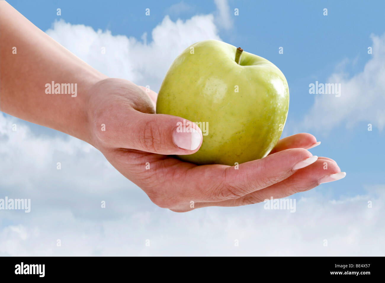 Hand holding a green apple against a blue sky Stock Photo