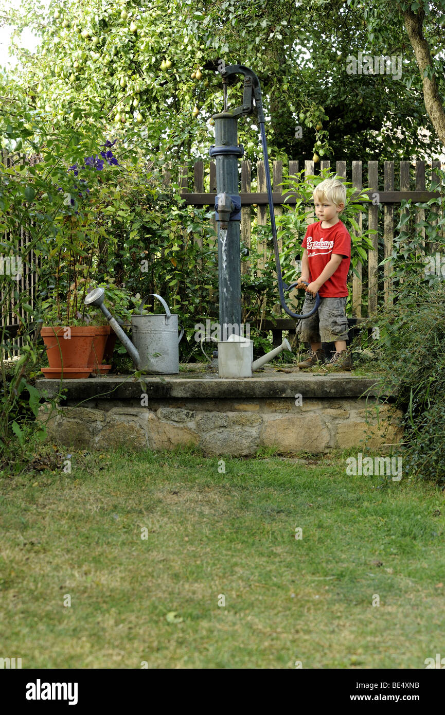 A Three Year Old Boy Plays With An Outdoor Vintage Hand Water Pump