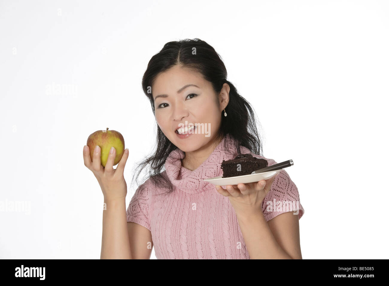 Cute Asian woman trying to make a decision between eating healthy or not Stock Photo