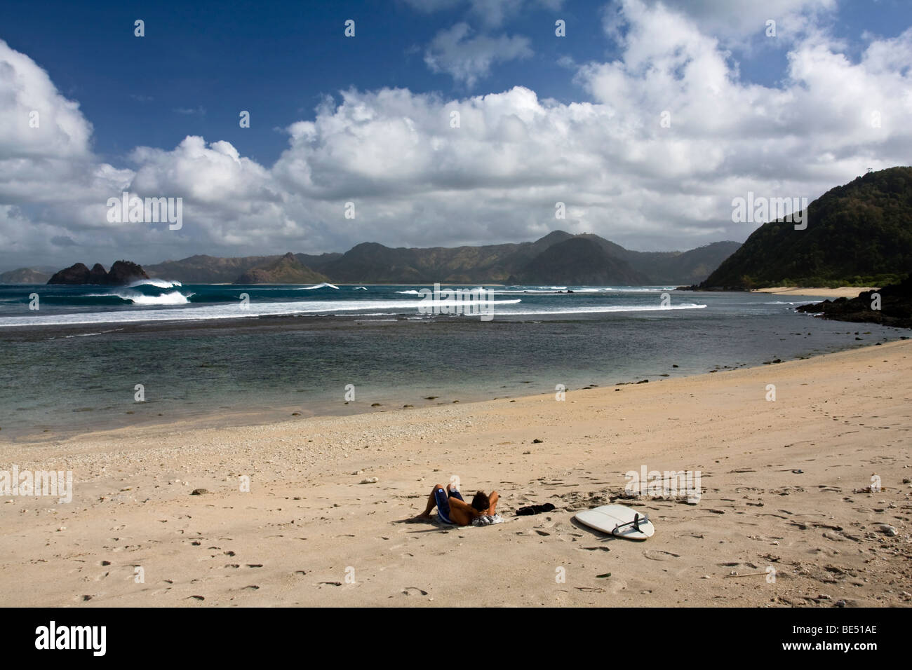 [surfing Lombok] Surfer lying on the beach relaxing with his surfboard