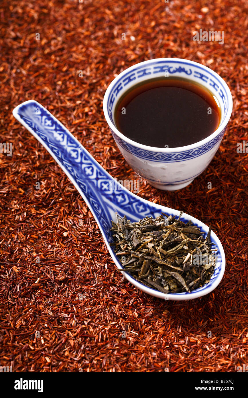 Black tea in an Asian teacup green tea leaves in an Asian spoon on a bed of tea leaves Stock Photo