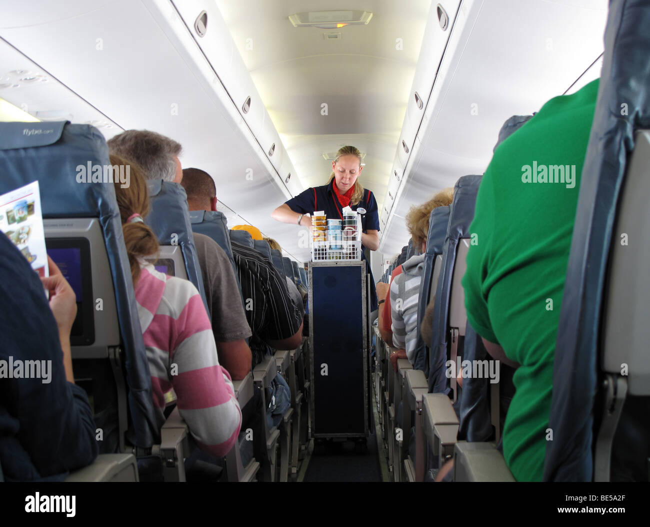 A female flight attendant or stewardess serves passengers on a FlyBe flight from Guernsey to London Gatwick Stock Photo