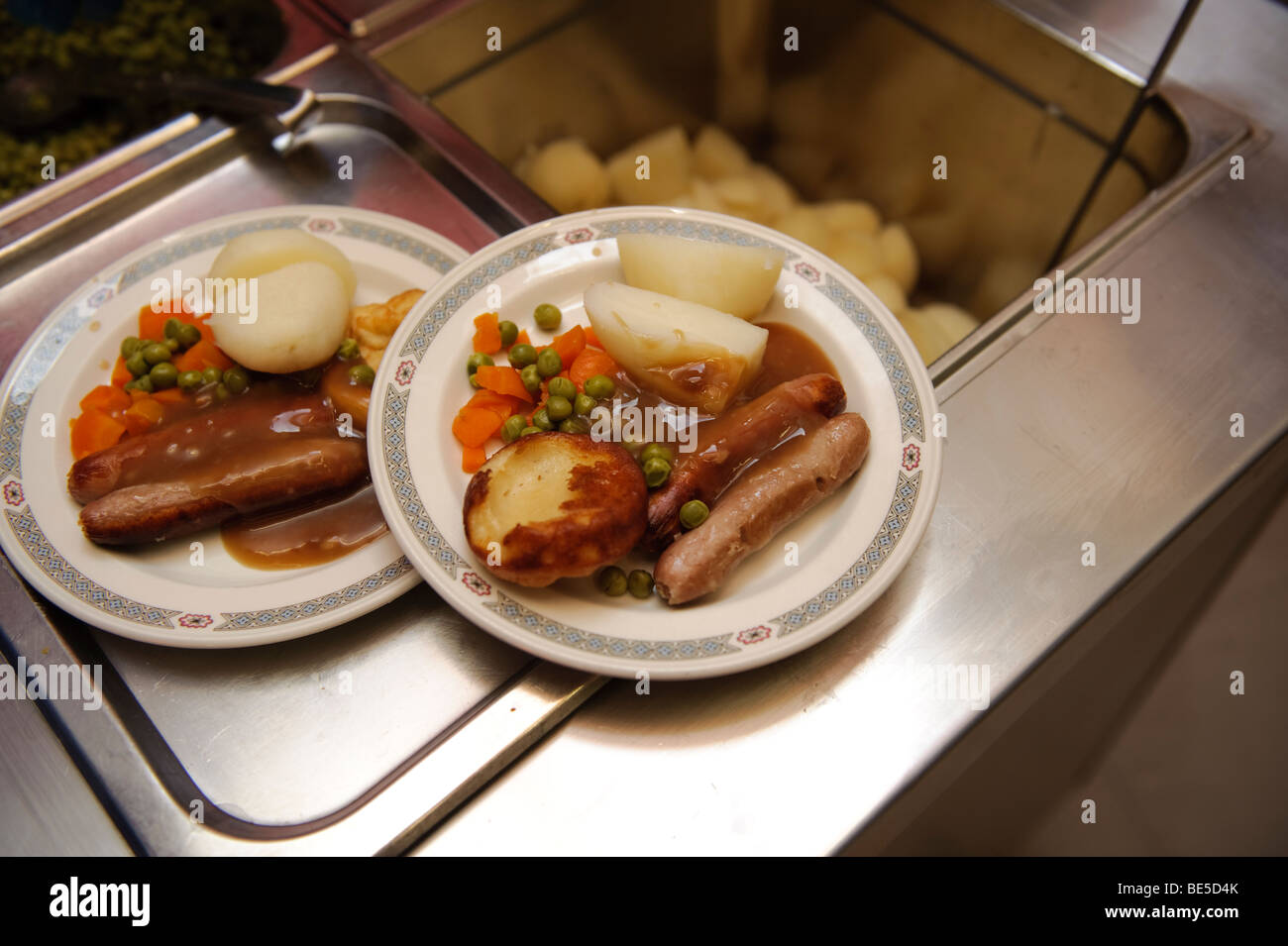 School dinners - sausage vegetables and potatoes -  served up on plates in a primary school canteen hall, Wales UK Stock Photo