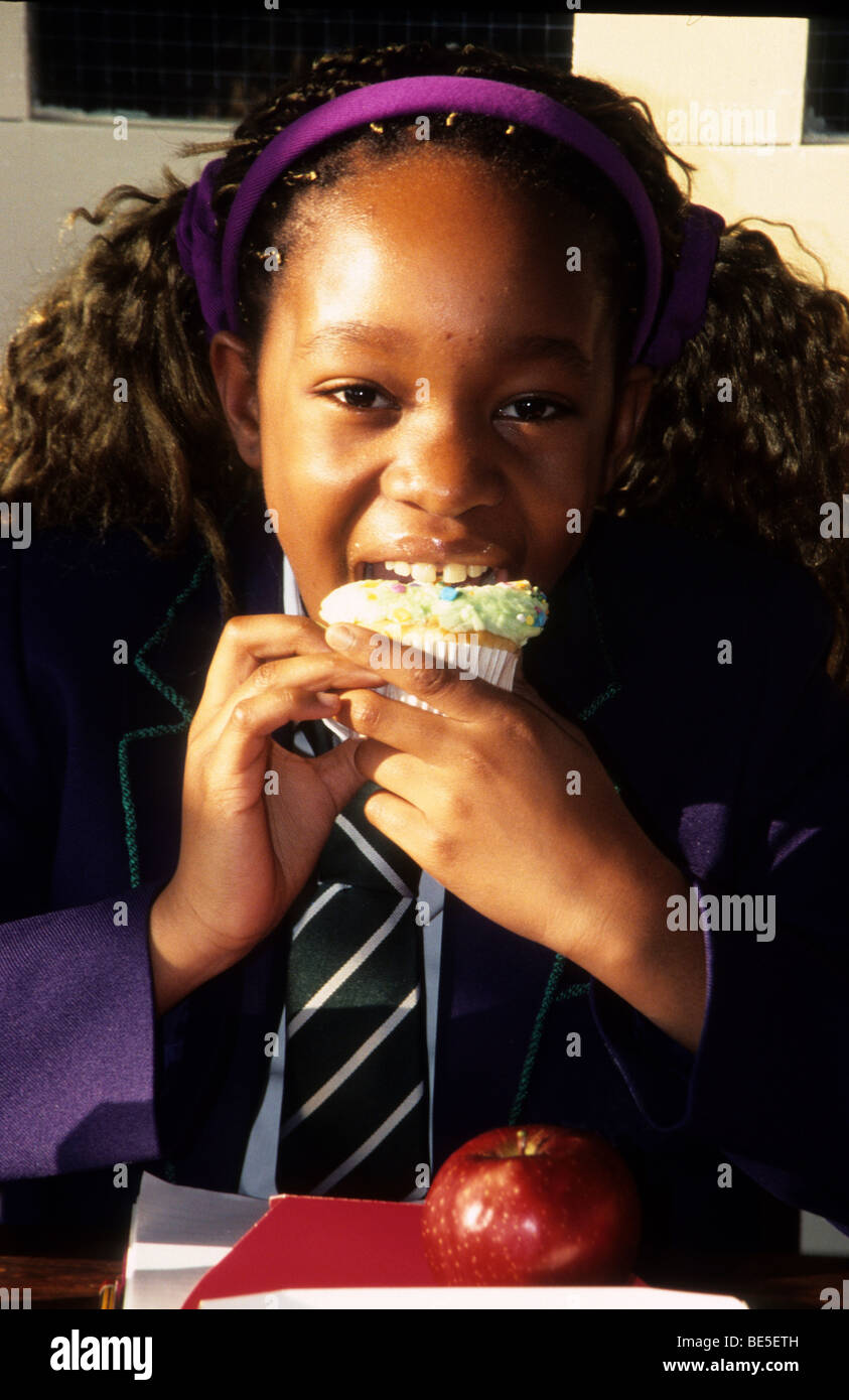 Pretty schoolgirl happily stuffing her face with a cupcake. Stock Photo