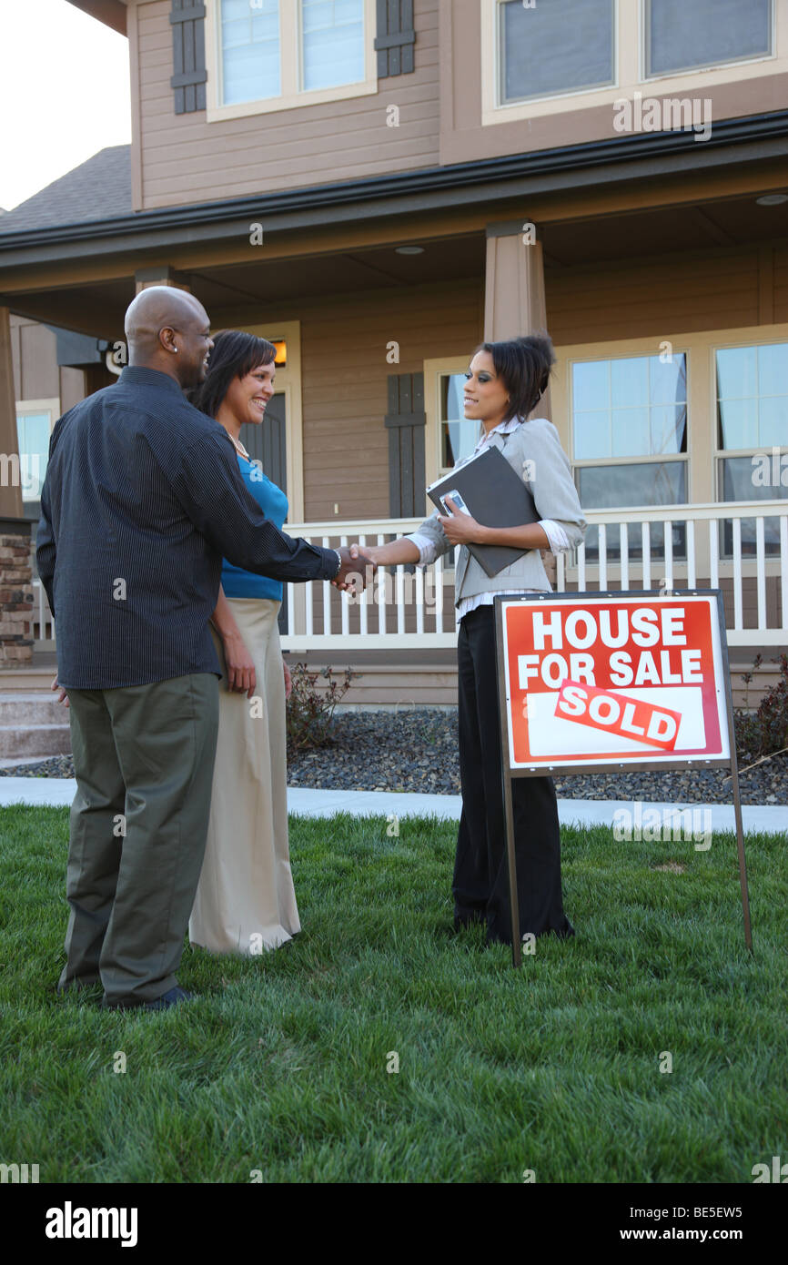 Couple shakes hands with Realtor in front of new home Stock Photo
