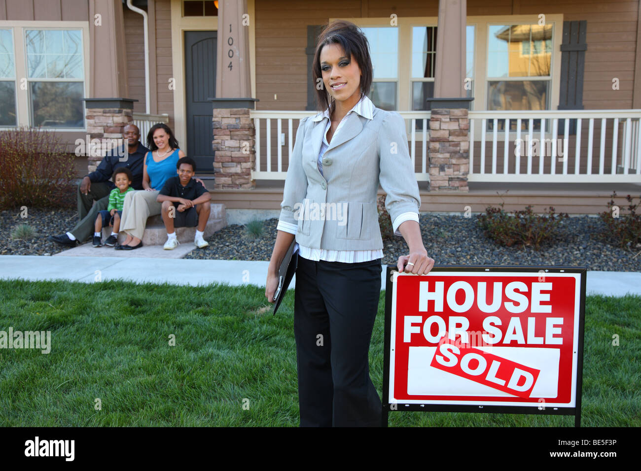 Realtor by sign with family in background on porch Stock Photo