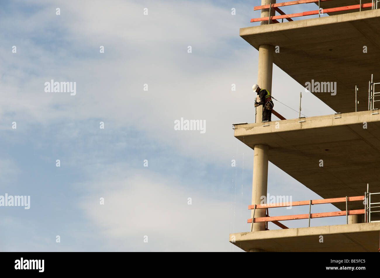 Construction worker fitting safety rails to s partly built office block ...
