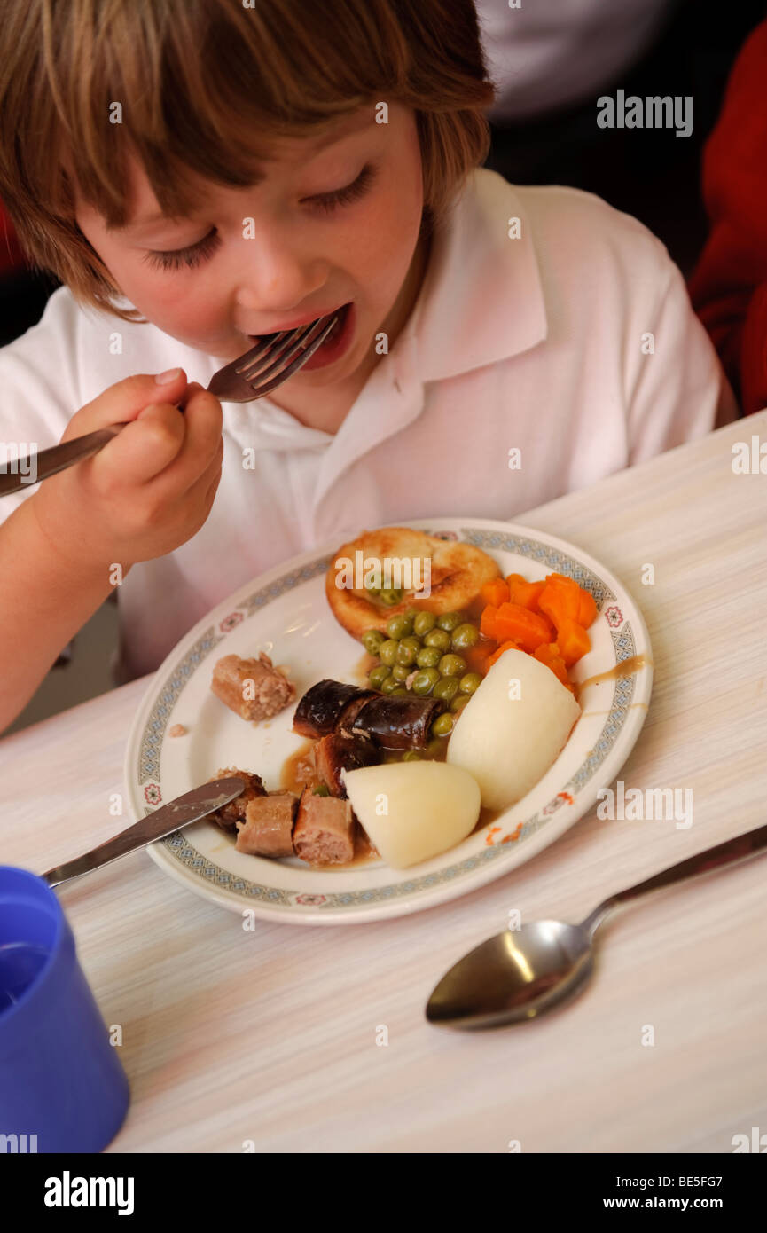 A Young boy child eating school dinner in a primary school canteen