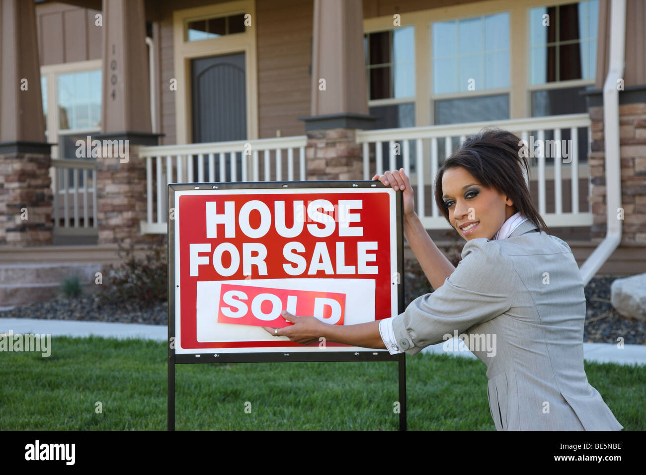 Female Realtor putting SOLD on sign in front of home Stock Photo