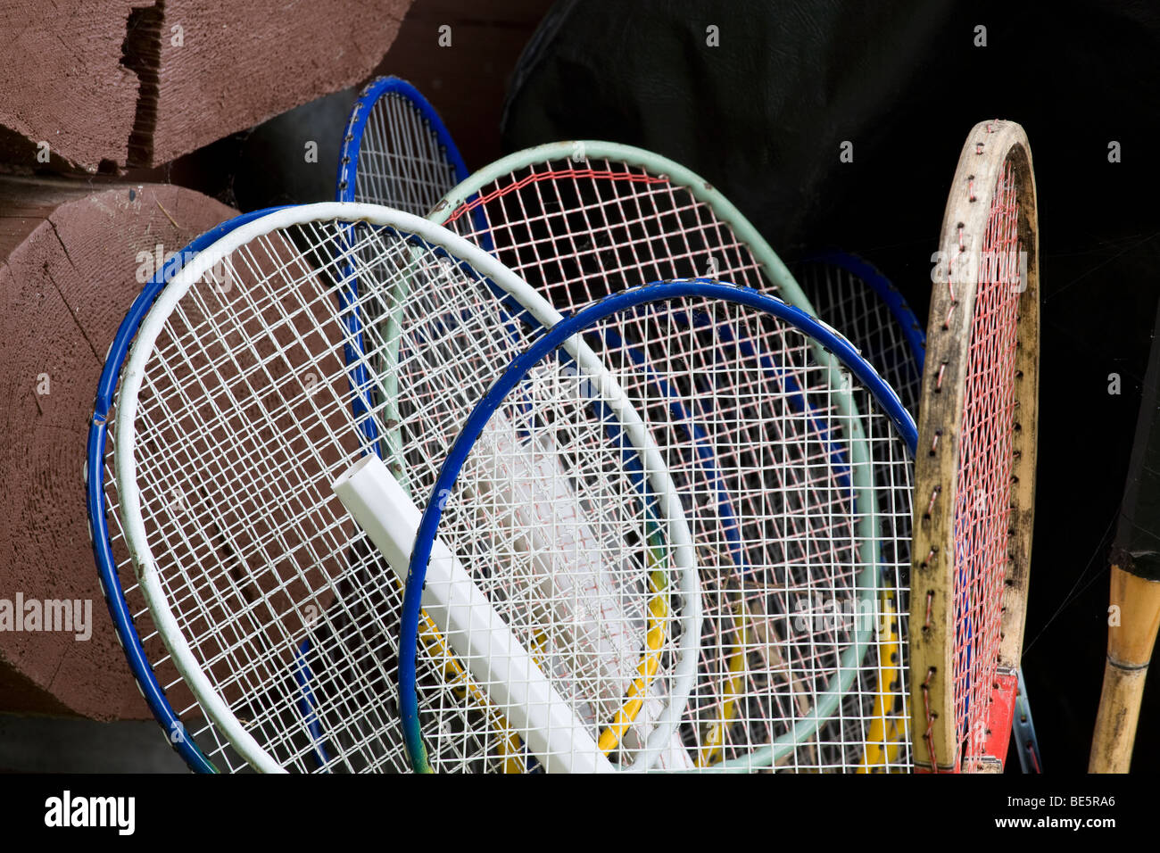 Badminton and Tennis Raquets. A collection of 6 badminton and one tennis raquet against the logs of a summer cottage or cabin. Stock Photo