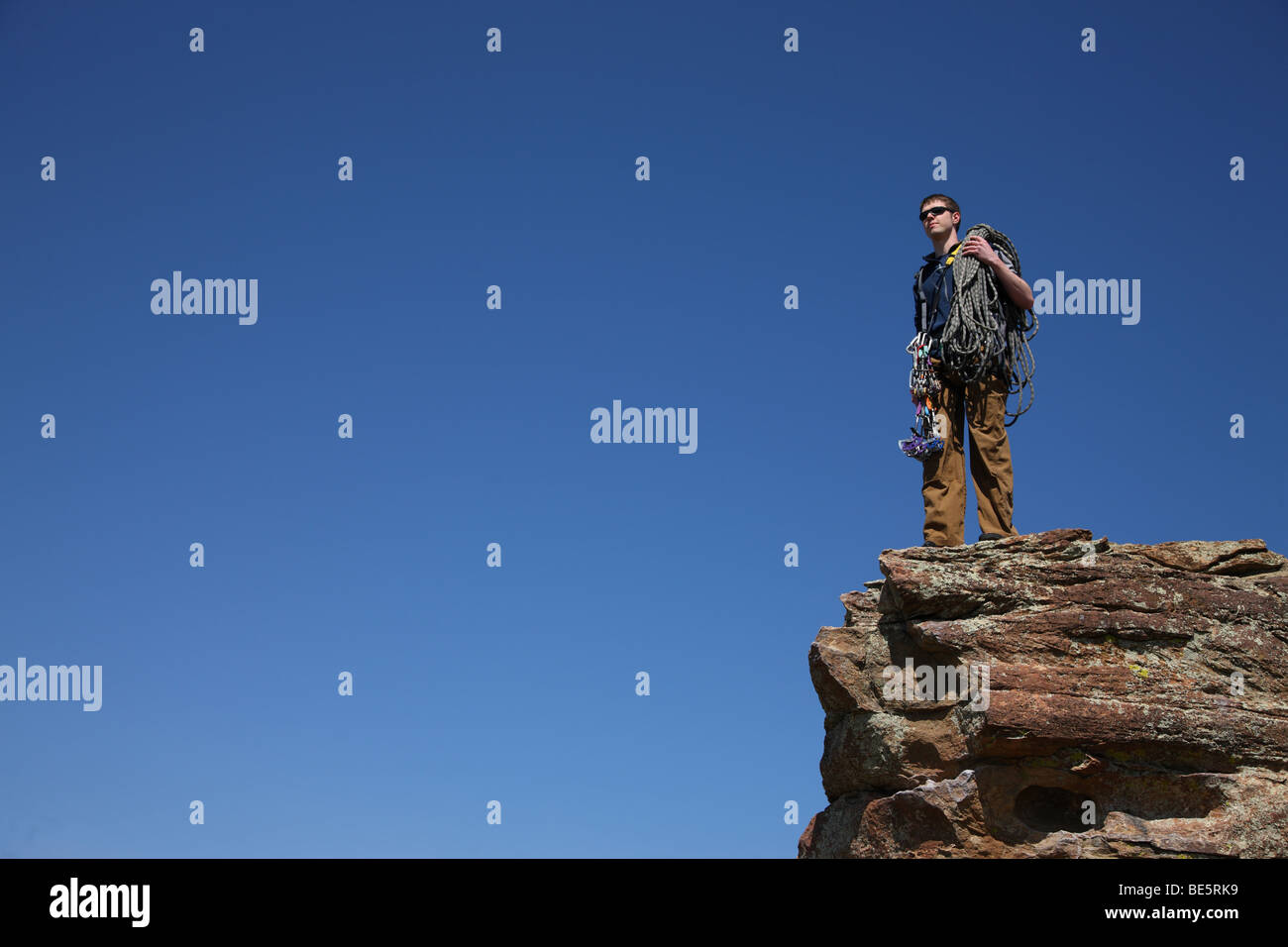 Climber stands on rocky cliff surrounded by blue sky Stock Photo