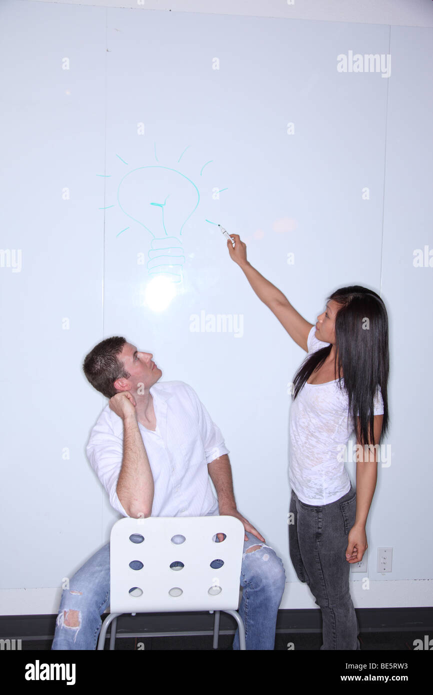 Woman writes on dry erase board as man looks up Stock Photo