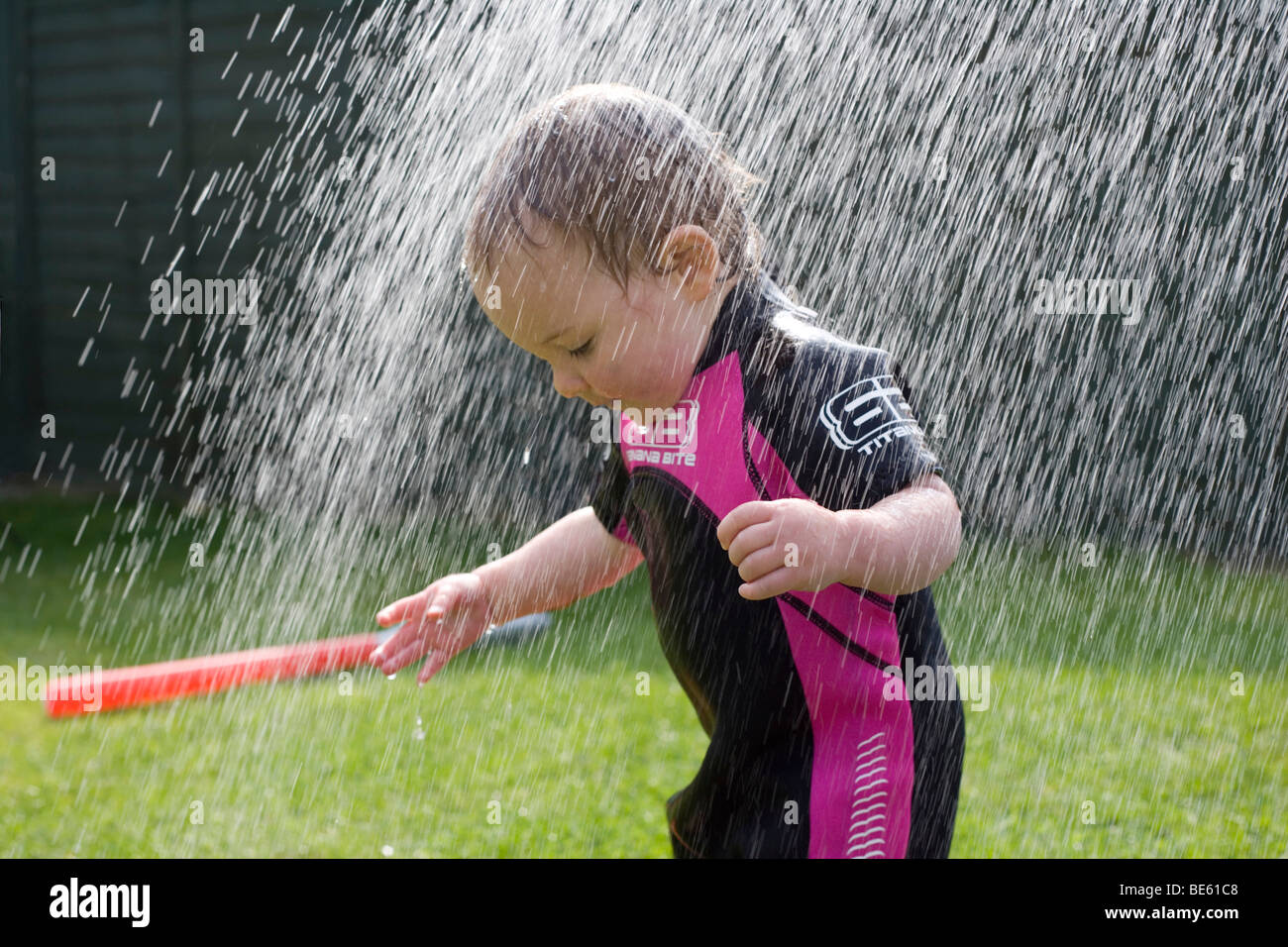 15 month old toddler in wetsuit under water spray Stock Photo